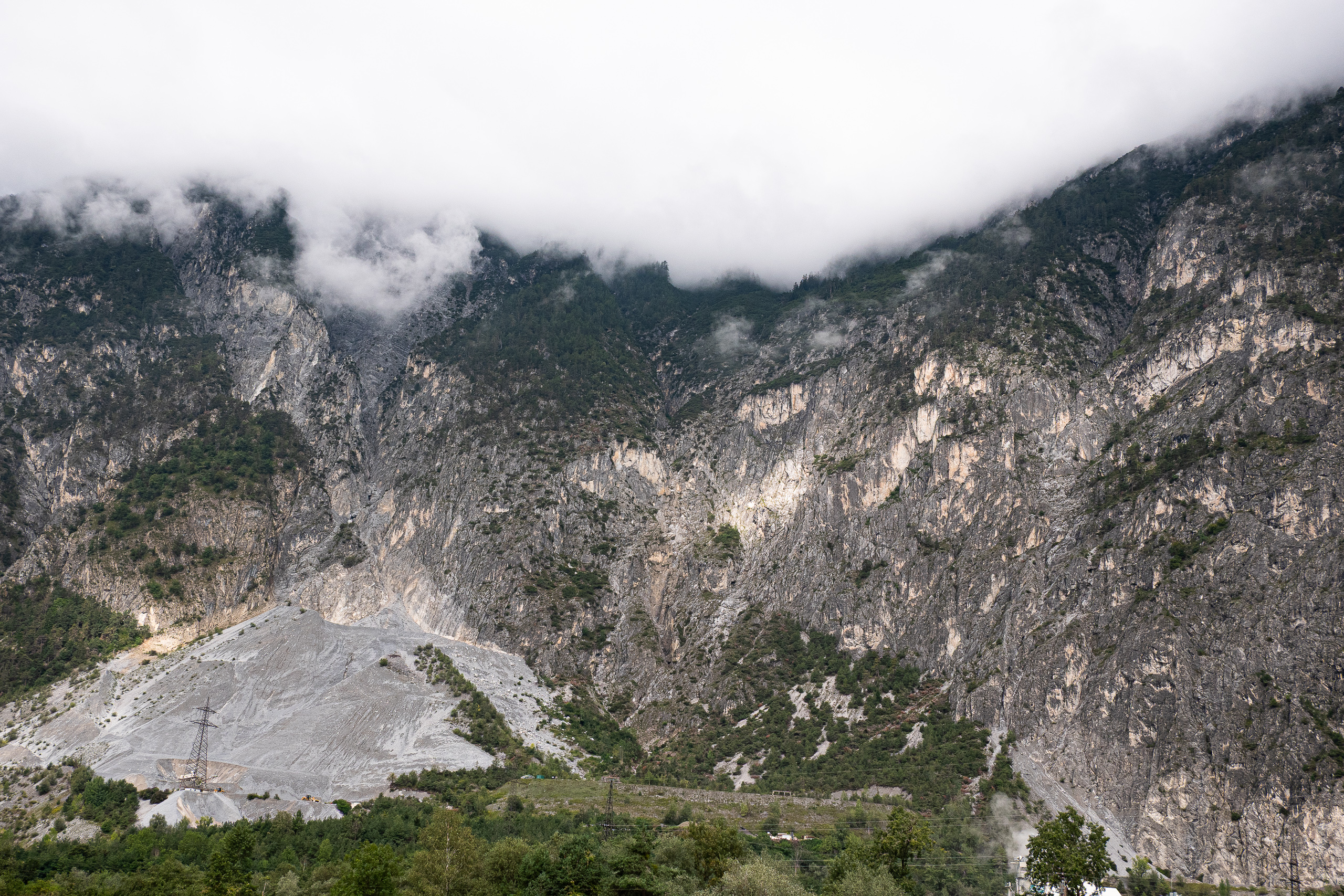Wolkenverhangene Felswände über einer Schutthalde im Oberinntal